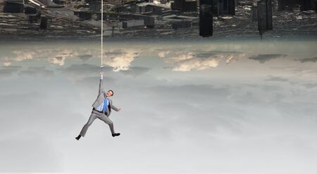 Young businessman hanging on rope above cityの写真素材