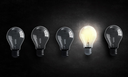 Light bulbs on dark background with one burning