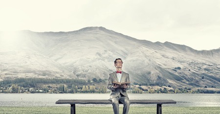 Young businessman wearing red bow tie sitting with book in handsの写真素材