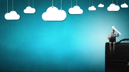 Young smiling businessman sitting on giant briefcaseの写真素材