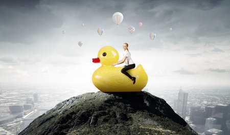 Young happy businesswoman riding yellow rubber duckの写真素材