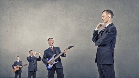 Young man in suit and people playing different music instrumentsの写真素材