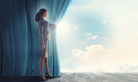 Young businesswoman opening stage curtain to another realityの写真素材