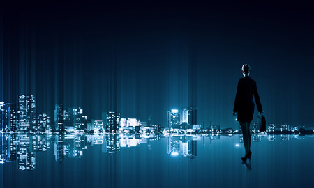 Businesswoman standing with back against night city panoramic viewの写真素材