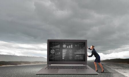 Young pretty businesswoman trying to move big laptopの写真素材