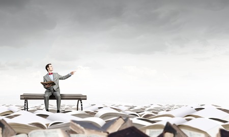 Young businessman wearing red bow tie sitting with book in handsの写真素材