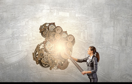Young businesswoman fixing gears mechanism with wrenchの写真素材