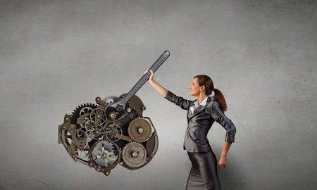 Young businesswoman fixing gears mechanism with wrenchの写真素材