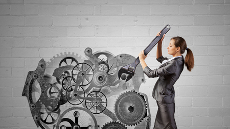 Young businesswoman fixing gears mechanism with wrenchの写真素材