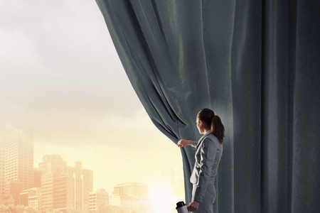 Young businesswoman opening stage curtain to another realityの写真素材