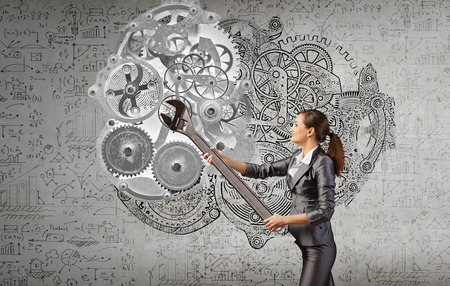 Young businesswoman fixing gears mechanism with wrenchの写真素材
