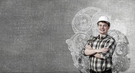 Portrait of happy mature architect in helmet standing with arms crossed on chestの写真素材