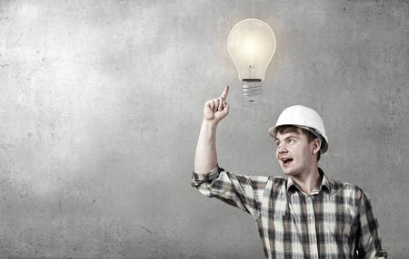 Young man builder looking thoughtfully at light bulb. Idea conceptの写真素材
