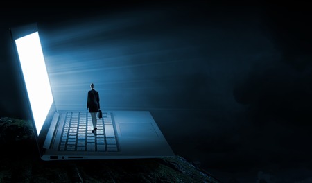 Rear view of businesswoman with suitcase standing on keyboard of big laptopの写真素材