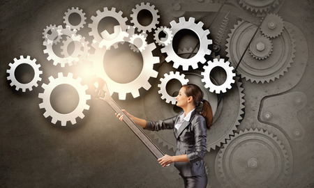 Young businesswoman fixing gears mechanism with wrenchの写真素材