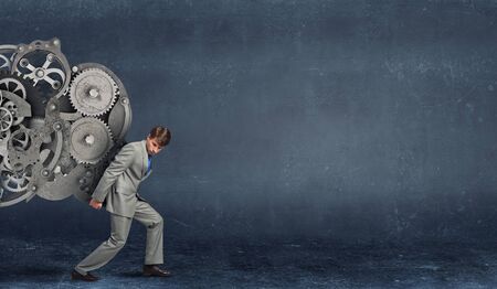 Young businessman carrying huge gears mechanism on backの写真素材