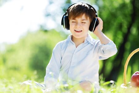 Young joyful boy in summer park wearing headphonesの写真素材