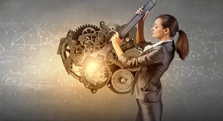 Young businesswoman fixing gears mechanism with wrenchの写真素材