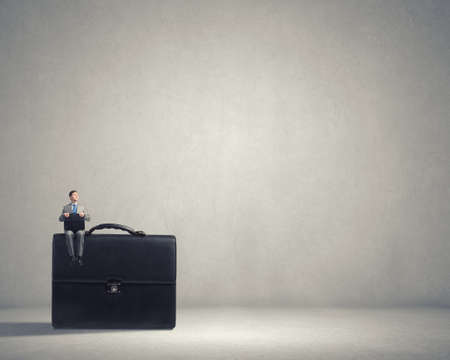 Young smiling businessman sitting on giant briefcaseの写真素材