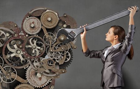 Young businesswoman fixing gears mechanism with wrenchの写真素材