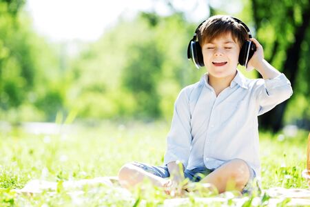 Young joyful boy in summer park wearing headphonesの写真素材