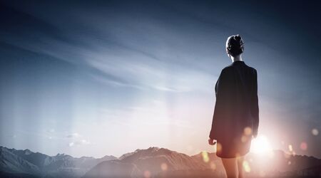 Back view of businesswoman against mountain landscape looking far awayの写真素材