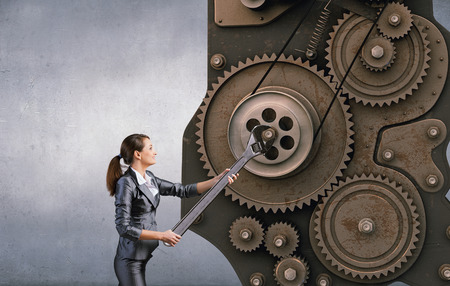 Young businesswoman fixing gears mechanism with wrenchの写真素材