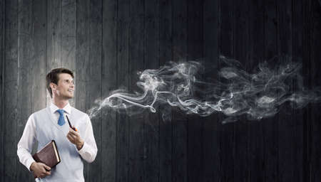Handsome young businessman thinking over ideas and smoking pipeの写真素材