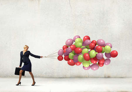 Young businesswoman with suitcase and bunch of colorful balloonsの写真素材
