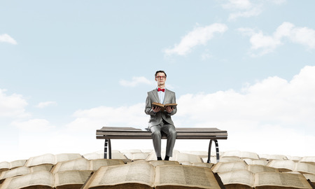 Young businessman wearing red bow tie sitting with book in handsの写真素材