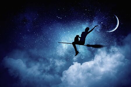 Happy young woman flying in sky on broomの写真素材