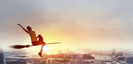 Happy young woman flying in sky on broomの写真素材