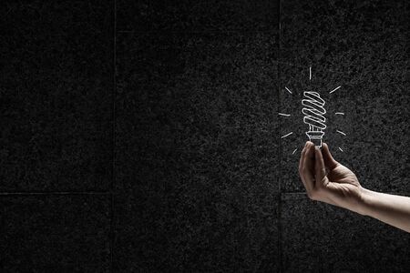 Human hand on dark background holding light bulbの写真素材
