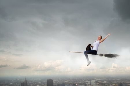 Happy young woman flying in sky on broomの写真素材