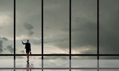 Businesswoman standing with back and looking in office windowの写真素材