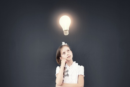 Cute thoughtful girl of school age standing near blackboardの写真素材