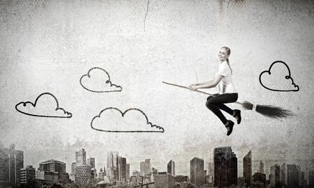 Happy young woman flying in sky on broomの写真素材
