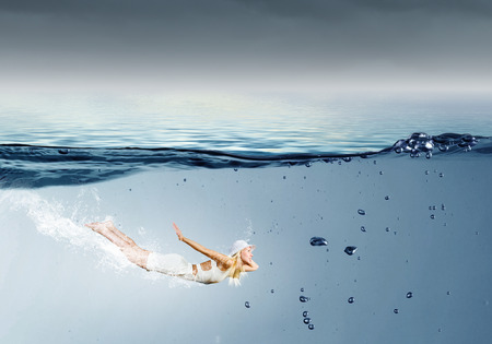 Young pretty girl in hat and dress swimming under waterの写真素材