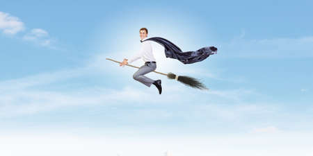 Young businessman flying on broom high in skyの写真素材