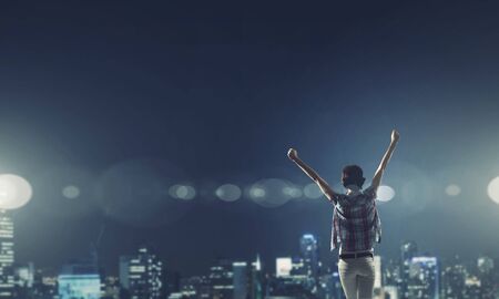 Rear view of young woman with hands up looking at night cityの写真素材