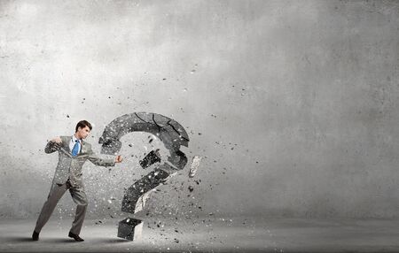 Young furious businesman crashing stone question markの写真素材