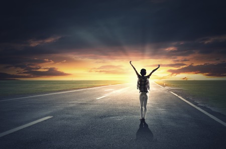 Rear view of girl with hands up facing sunriseの写真素材