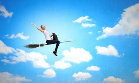 Young girl in casual flying on broom high in skyの写真素材