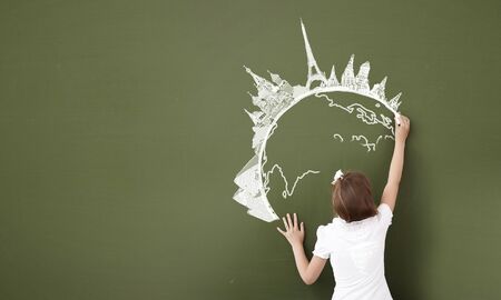 Cute girl of school age writing with chalk on blackboardの写真素材