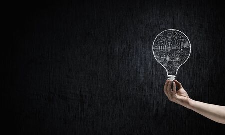 Human hand on dark background holding light bulbの写真素材