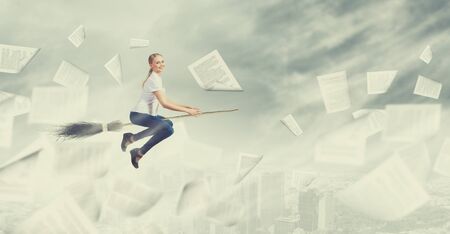 Young girl in casual flying on broom high in skyの写真素材