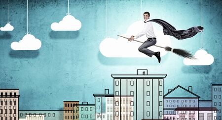 Young businessman flying on broom high in skyの写真素材