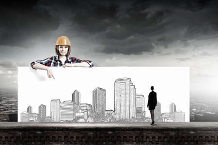 Young woman builder wearing helmet and holding banner with construction sketchesの写真素材