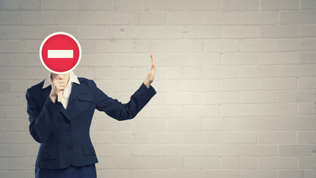 Unrecognizable businesswoman hiding her face behind stop signの写真素材