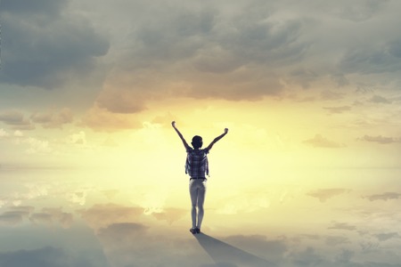 Rear view of girl with hands up facing sunriseの写真素材